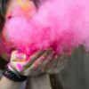 Eine Frau blässt aus ihren Händen eine Wolke rosa Staub.