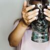 Frau hält Flasche geformt als Kopf vor Gesicht