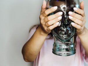 Frau hält Flasche geformt als Kopf vor Gesicht