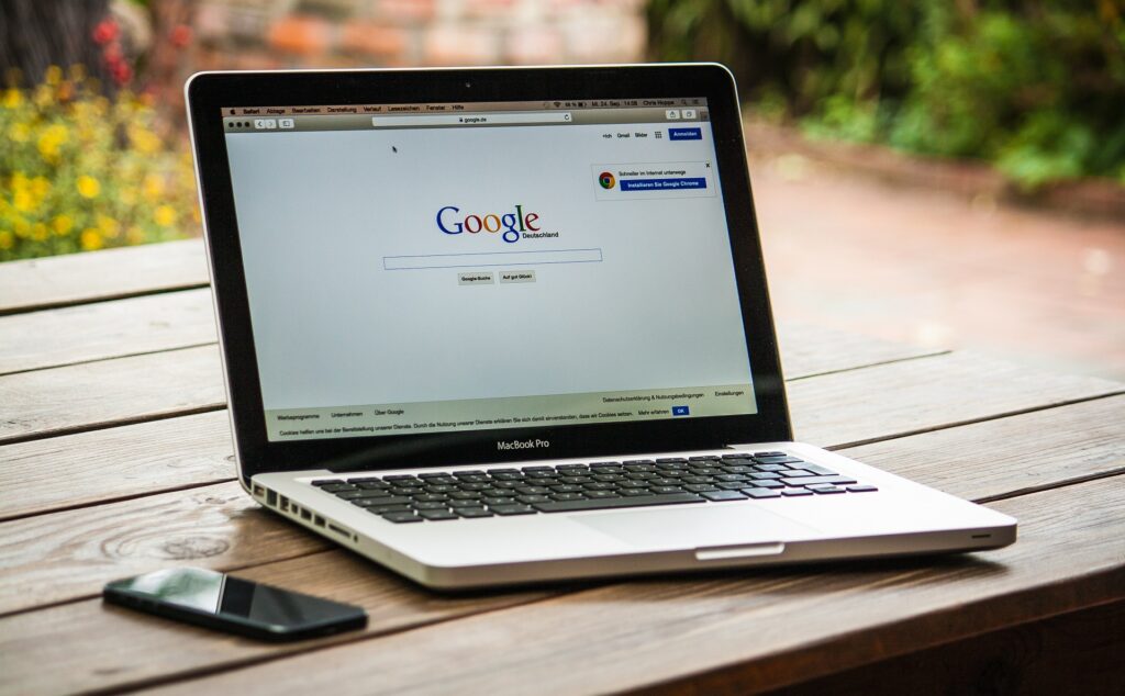 Macbook auf dem Google steht und Handy auf Holztisch