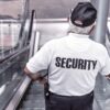 Mann auf Rolltreppe mit Rücken zur Kamera. Weißes Shirt auf dem Security steht. Blog Paragraph 13