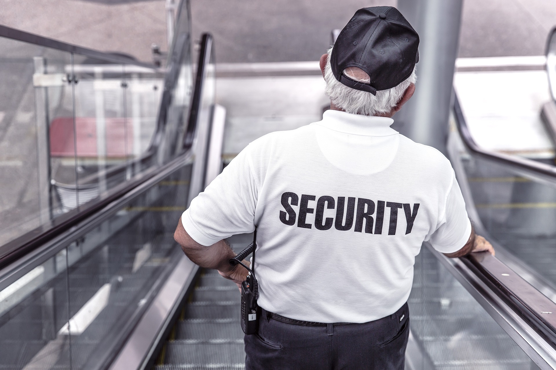 Mann auf Rolltreppe mit Rücken zur Kamera. Weißes Shirt auf dem Security steht. Blog Paragraph 13