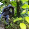 Figur eines Mannes, der auf einer Mauer sitzt, sich herunter beugt und durch ein Fernglas schaut.