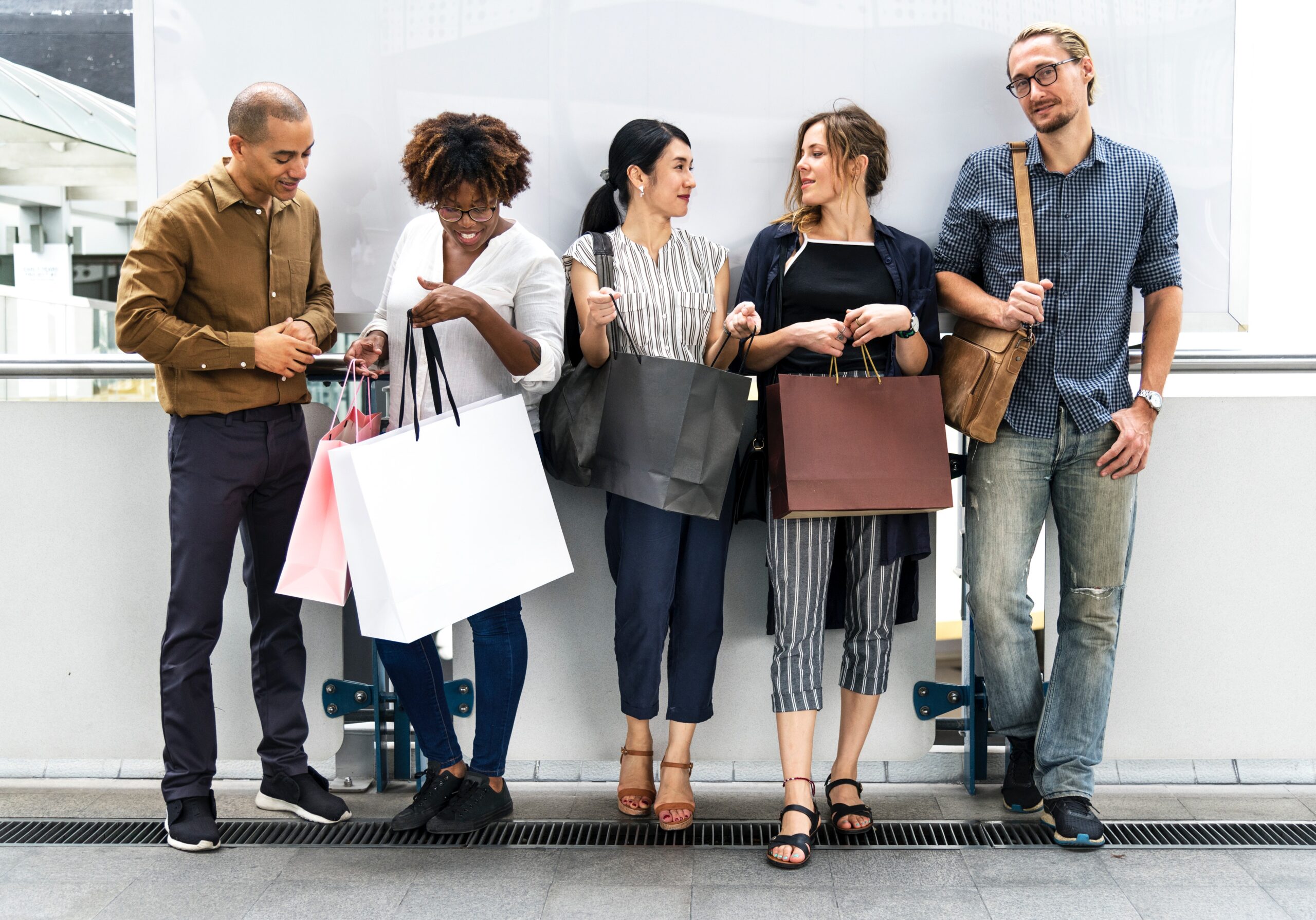 Fünf glückliche Leute mit Shoppingtüten vor weißer Wand