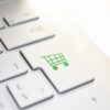 Ausschnitt einer weißen Tastatur, auf deren Enter-Taste sich ein grüner Einkaufswagen befindet.