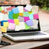Ein Smartphone und ein Laptop mit Post-Its auf dem Bildschirm befinden sich auf einem Tisch