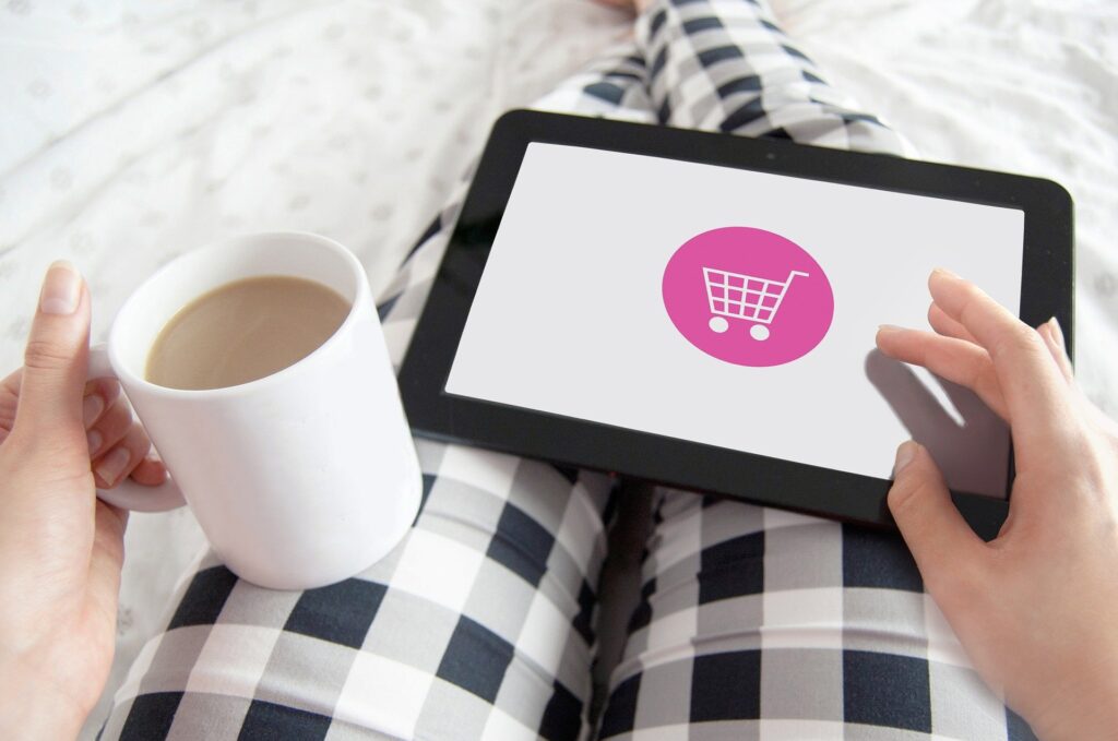 Frau liegt mit Kaffee und einem Tablet auf dem Bett