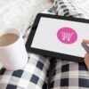 Frau liegt mit Kaffee und einem Tablet auf dem Bett