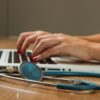 Frau tippt auf Macbook daneben liegt Stethoskop - Blog: SEO für Ärzte