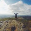 Mann steht auf Berg und blickt auf Landschaft. Sinnbild für den Blogbeitrag Wie kommt man bei Google nach oben