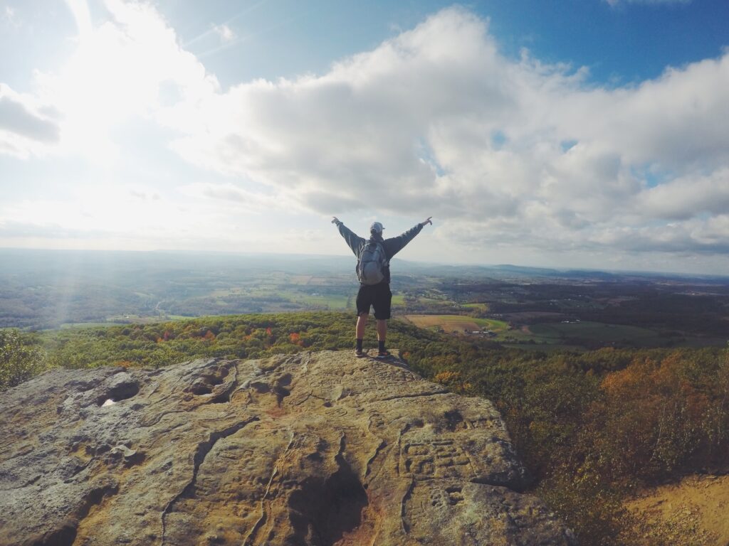 Mann steht auf Berg und blickt auf Landschaft. Sinnbild für den Blogbeitrag Wie kommt man bei Google nach oben