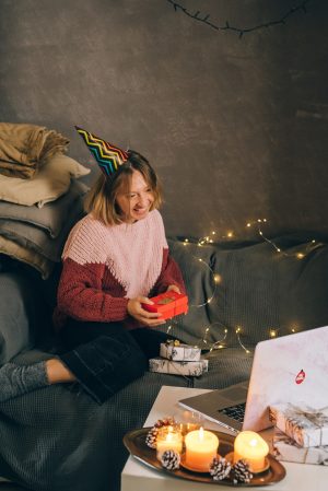 Frau sitzt auf Sofa vor dem Laptop mit Geschenk in der Hand - Blog: Virtuelle Weihnachtsfeier