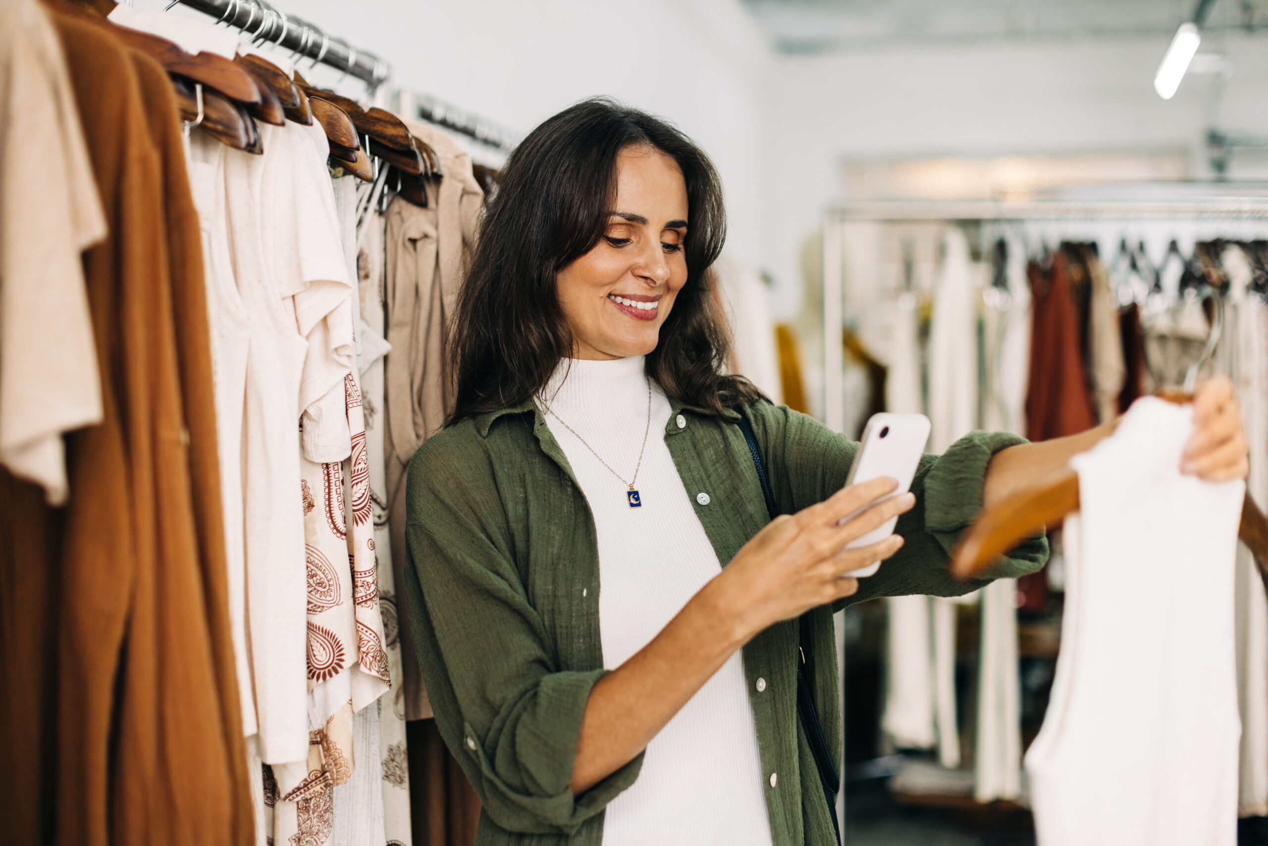 Frau fotografiert Kleidungsstück im Laden mit Smartphone